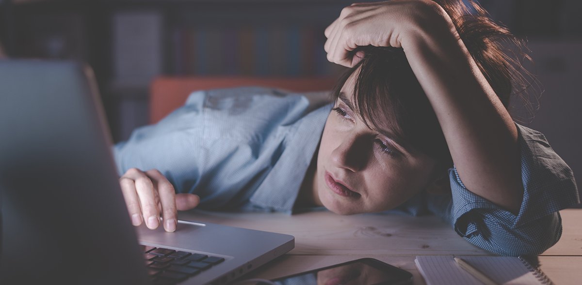 Eine müde Frau, die mit ihrem Laptop am Schreibtisch arbeitet und dabei fast einschläft