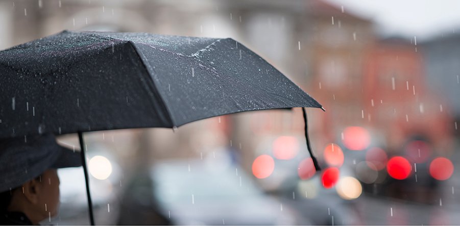 Ausschnitt einer Frau mit einem schwarzen Regenschirm, der Hintergrund ist unscharf dargestellt mit roten Blindpunkten